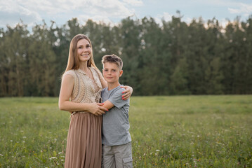 A beautiful young mother hugs her son on a green lawn. Family concept, child-rearing, mother-son...