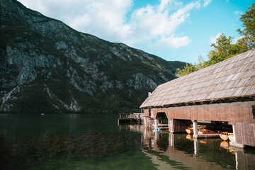 Lake Bohinj boathouse with mountain backdrop under a cloudy sky.