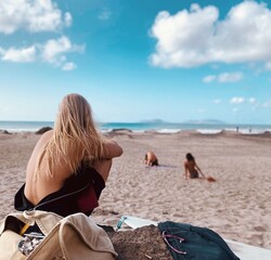 “Young blonde female surfer gazing at the ocean under Famara cliffs, Lanzarote”