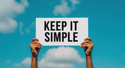 Hands Holding Sign with 'Keep It Simple' Message Against a Blue Sky Background