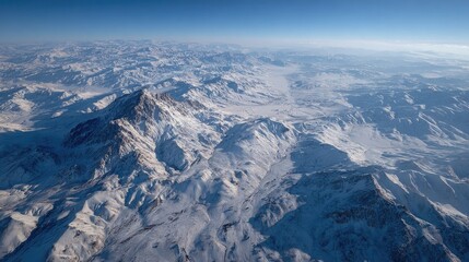 Aerial view of snow-capped mountain range. Vast, icy peaks stretch across the frame, a panorama of rugged, pristine landscapes under a clear sky