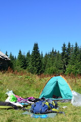 a tent with camping gear in front of a forest in the mountains