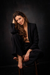 Brunette haired woman wearing black blazer and posing against at isolated dark background