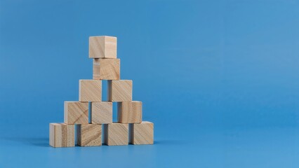 Depiction of development in business and personal skills shown through a wooden cube pyramid balanced on an uneven base, set on a blue background with empty space. Benchmarking concept.