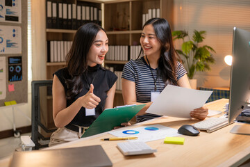 Fototapeta premium Two women are sitting at a desk with papers and a computer monitor