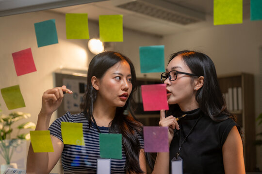 Two women are looking at a board with colorful sticky notes on it