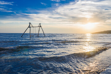  Sunset view at Velika Plaza beach in Ulcinj, Montenegro, with wooden swings standing in the sea. Gentle waves reflect golden light under a vivid blue and orange sky.