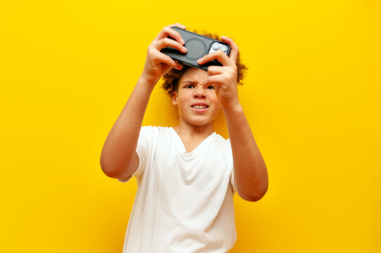 cheerful african american boy in white t-shirt playing video games on smartphone over yellow isolated background and smiling, curly schoolboy using phone for mobile games
