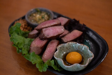 Grilled beef tongue served on plate with pickled egg yolk and sauce