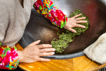 Working pressing the fresh longjing tea leaves in a pan to flatten the leaves as second step in...