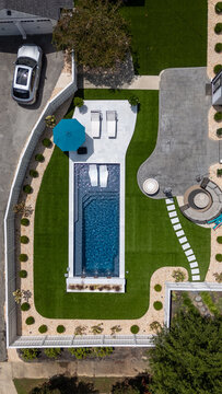 Vertical top down aerial drone view of a luxury backyard swimming pool and patio in summer