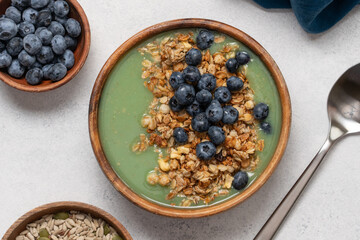Healthy Green Smoothie Bowl with Granola and Blueberries in Wooden Bowl on White Background