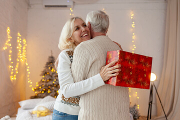 couple of elderly seniors in sweaters celebrate new year at home and hug, gray-haired old...