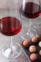 Tasty truffle bonbons and red wine on grey textured table, closeup