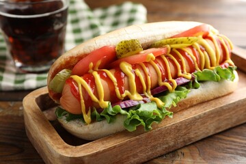 Tasty hot dog and soda drink on wooden table, closeup