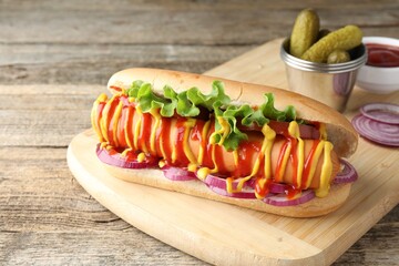 Tasty hot dog with vegetables, mustard and ketchup on wooden table, closeup