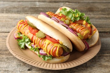 Tasty hot dogs with vegetables, mustard and ketchup on wooden table, closeup