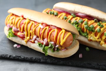 Delicious hot dogs with sauces, lettuce and onion on grey table, closeup