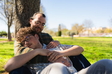 Happy gay couple embracing and relaxing under a tree in a peaceful urban park