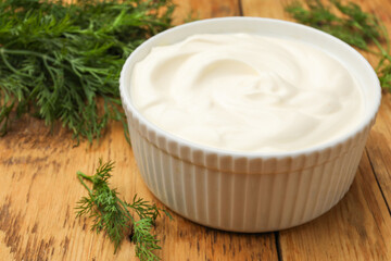 Tasty sour cream in bowl and dill on wooden table, closeup