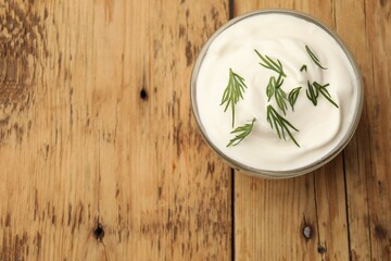 Tasty sour cream in bowl and dill on wooden table, top view. Space for text