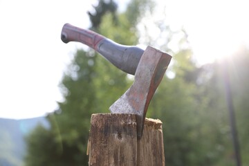 Metal axe on wooden log outdoors, closeup