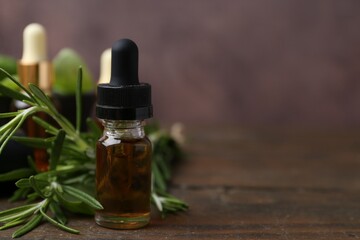 Bottles of aromatic essential oils and herbs on wooden table against brown background, closeup....