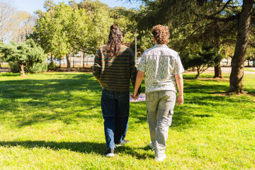 Fototapeta premium Romantic gay couple holding hands walking on grass in a park on a sunny day
