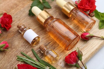 Bottles of essential oils, red roses and herbs on table, closeup