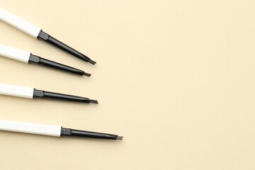 Automatic eyebrow pencils on beige background, flat lay. Space for text
