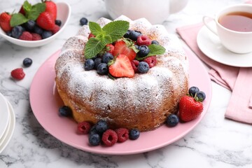 Tasty Bundt cake with powdered sugar and berries on white marble table, closeup