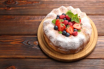 Tasty Bundt cake with powdered sugar and berries on wooden table, space for text