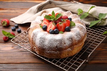 Tasty Bundt cake with powdered sugar and berries on wooden table, closeup