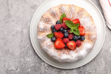 Tasty Bundt cake with powdered sugar and berries on grey textured table, top view