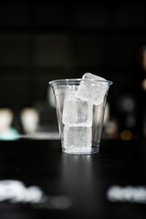 Fili of three square ice cubes in empty glass on black table
