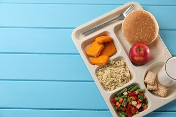 School lunch. Plastic tray with tasty food, milk and fork on light blue wooden table, top view. Space for text