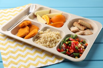 Plastic tray with tasty food and fork on light blue wooden table, closeup. School lunch