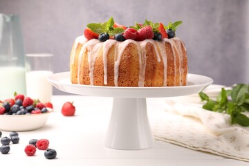 Delicious bundt cake with berries, glaze and mint on white wooden table against grey background,...