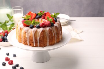 Delicious bundt cake with berries, glaze and mint on white wooden table against grey background, closeup
