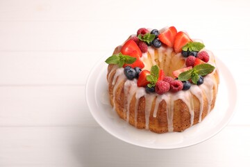 Delicious bundt cake with berries, glaze and mint on white wooden table, closeup. Space for text