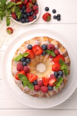Delicious bundt cake with berries, glaze and mint on white wooden table, flat lay