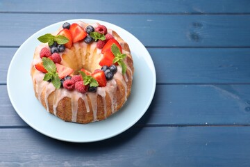 Delicious bundt cake with berries, glaze and mint on blue wooden table