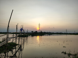 Fototapeta premium Rural Sunset Over Water Man On Bamboo Bridge Electricity Pylon Silhouette