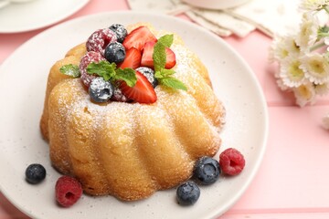 Delicious bundt cake with powdered sugar, berries and mint on pink wooden table, closeup