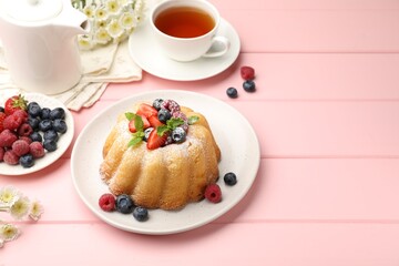 Delicious bundt cake with powdered sugar, berries, mint and tea on pink wooden table