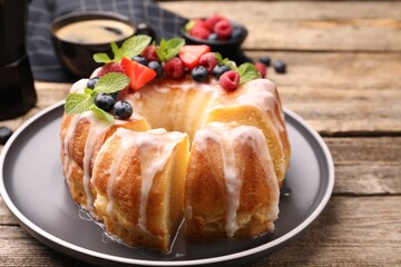 Pieces of delicious bundt cake with berries, glaze and mint on wooden table, closeup