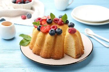 Tasty Bundt cake with berries, honey and mint on light blue wooden table, closeup