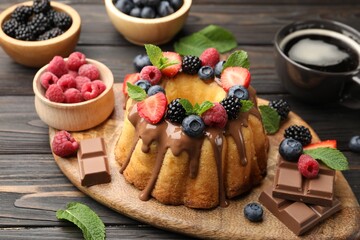 Tasty Bundt cake with berries, chocolate, mint and coffee on wooden table, closeup