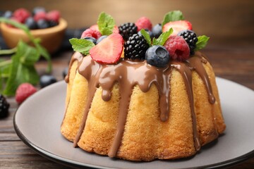 Tasty Bundt cake with berries, chocolate and mint on wooden table, closeup