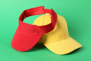 Yellow baseball and red visor caps on green background, closeup. Mockup for design